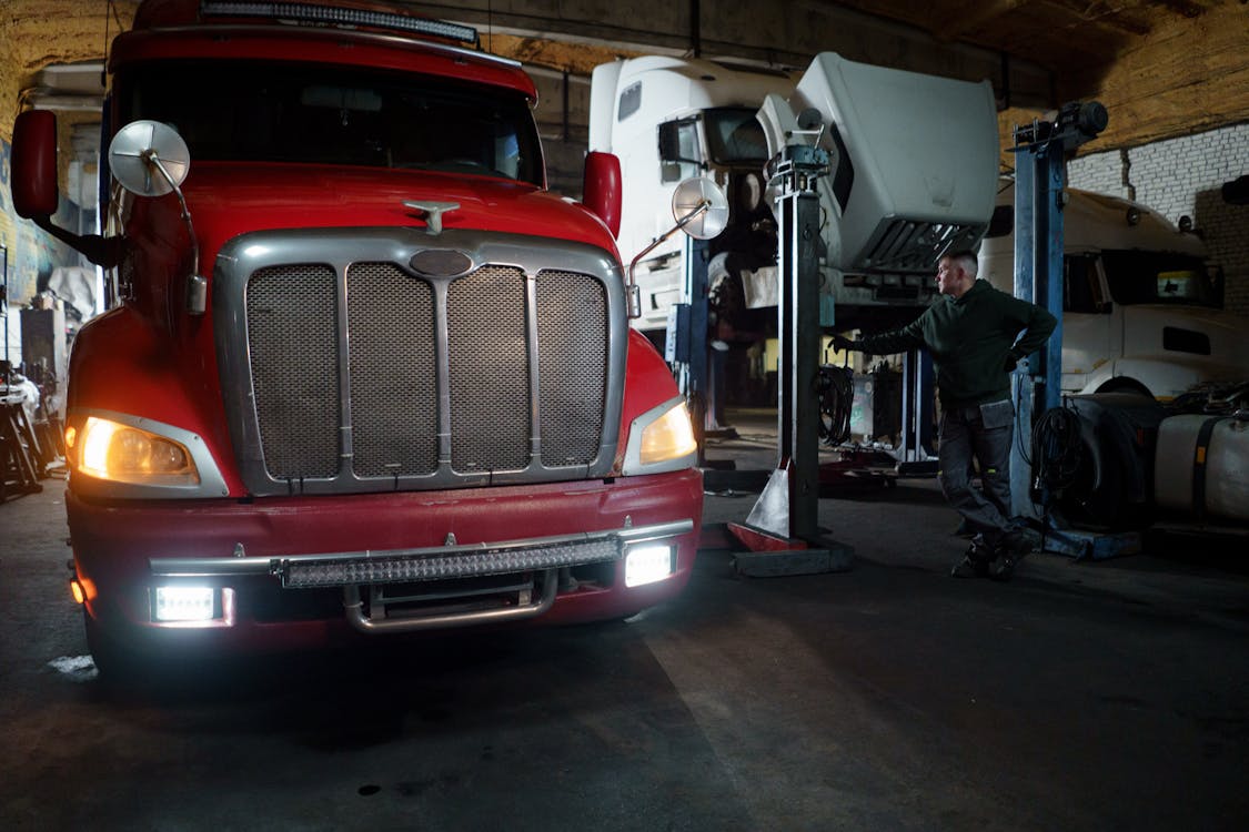 mechanic working in garage with two trucks, one truck on lift, the other on the ground